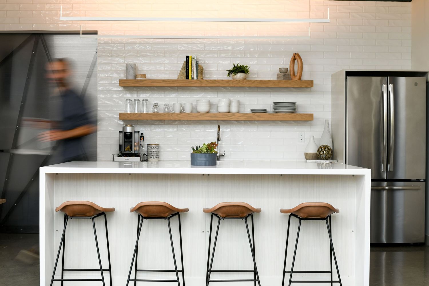 Modern minimalist kitchen with white counter and four wooden barstools.