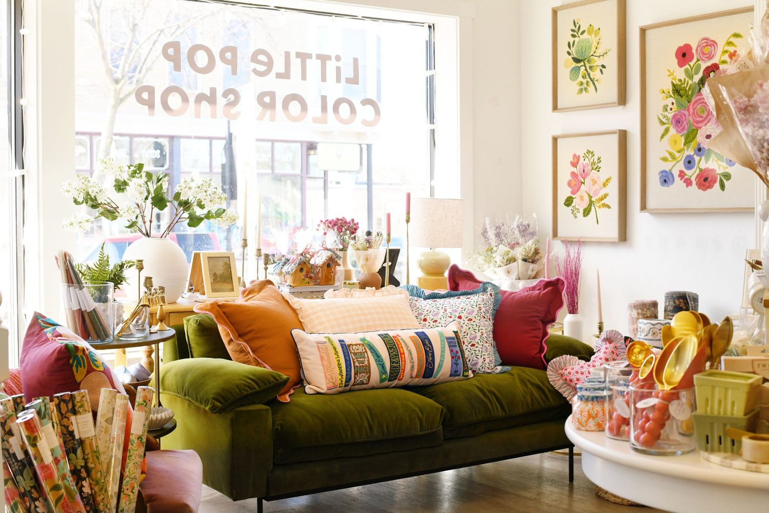 Cozy living room with olive green velvet sofa, colorful pillows, and botanical art prints on the wall.