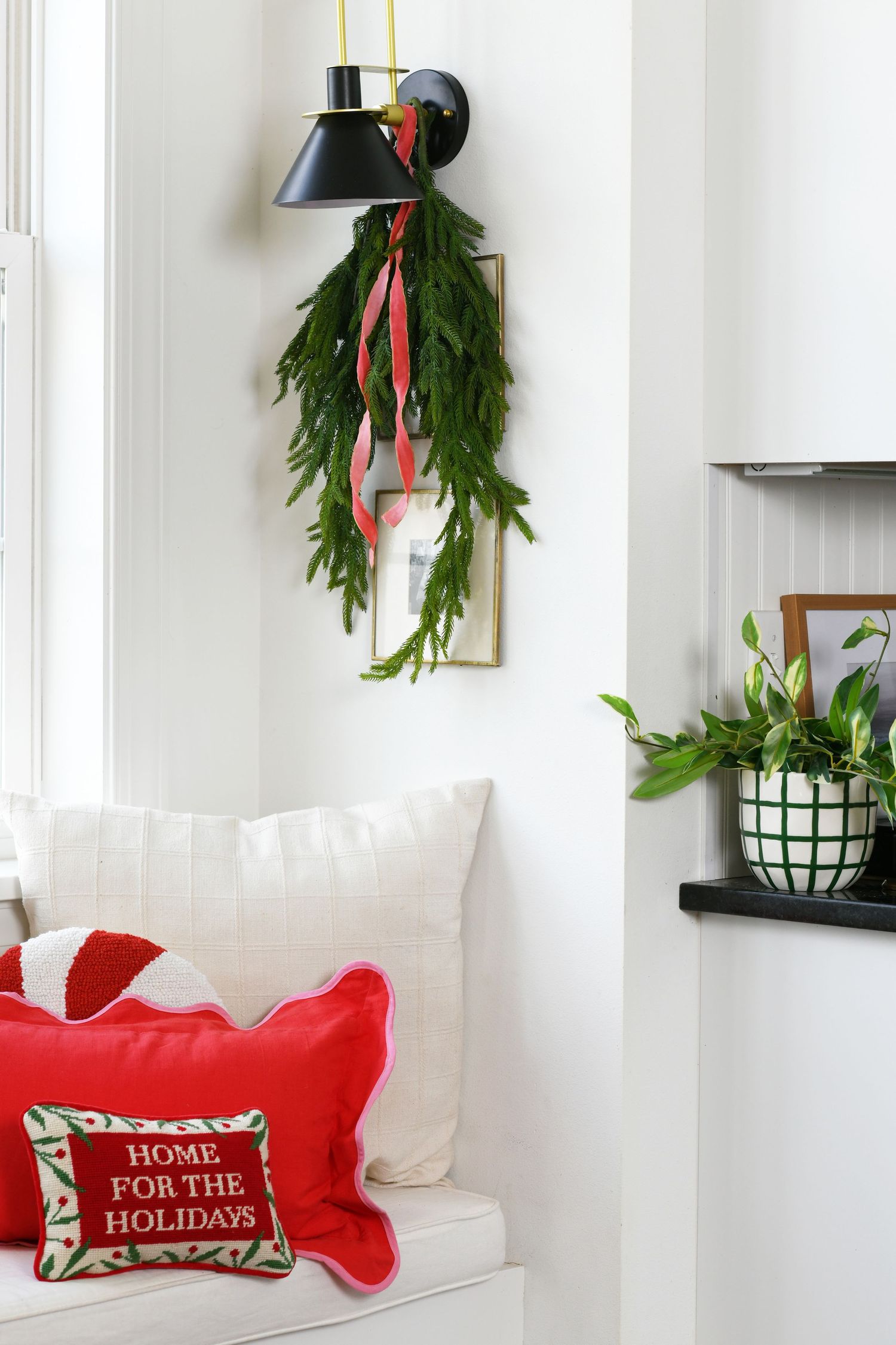 Wall-mounted sconce with fresh evergreen garland and red ribbon hanging below white throw pillows.