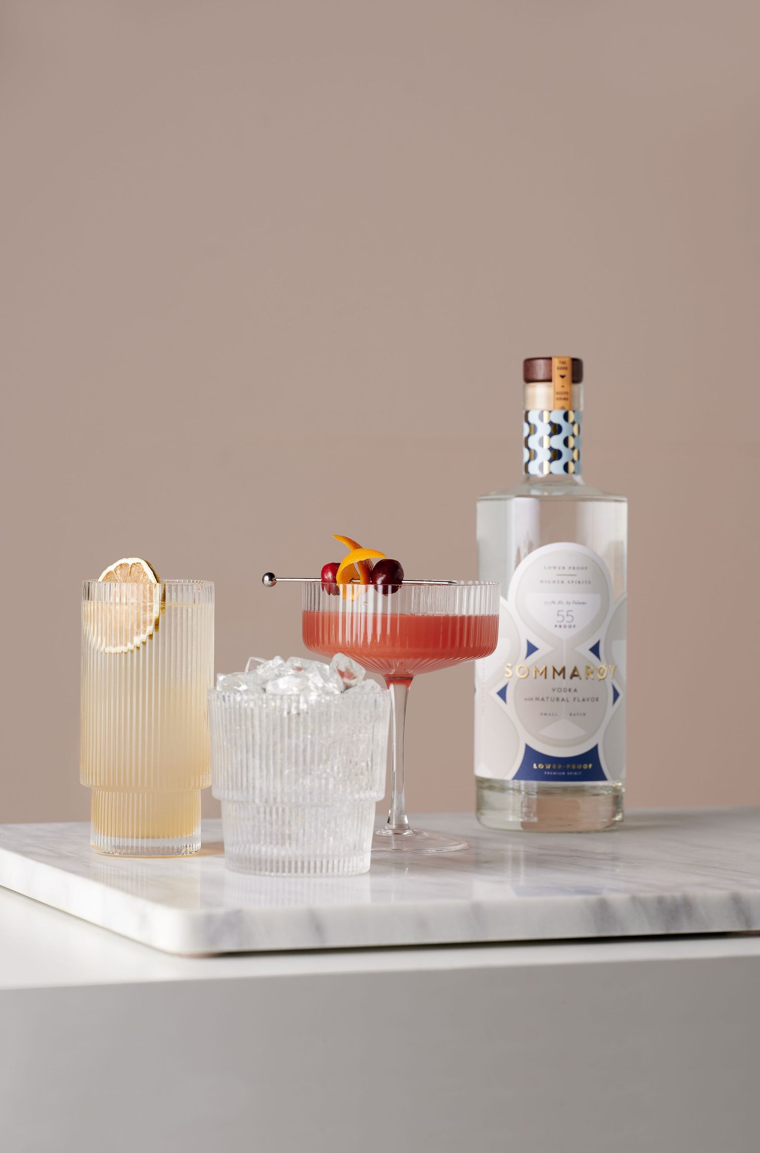 Elegant cocktail set featuring three different drinks and a white bottle on marble surface.