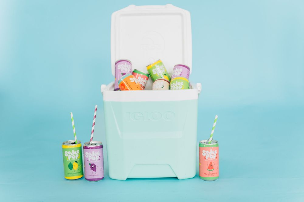 Colorful canned drinks arranged on a light blue background with a white cooler box.