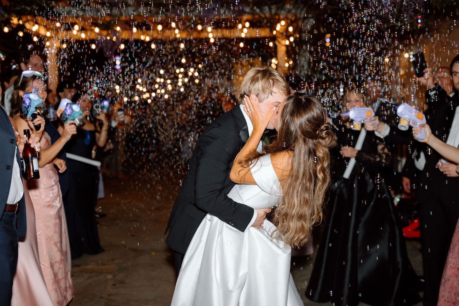 Bride and groom share a romantic kiss during a bubble send-off at their elegant wedding reception.