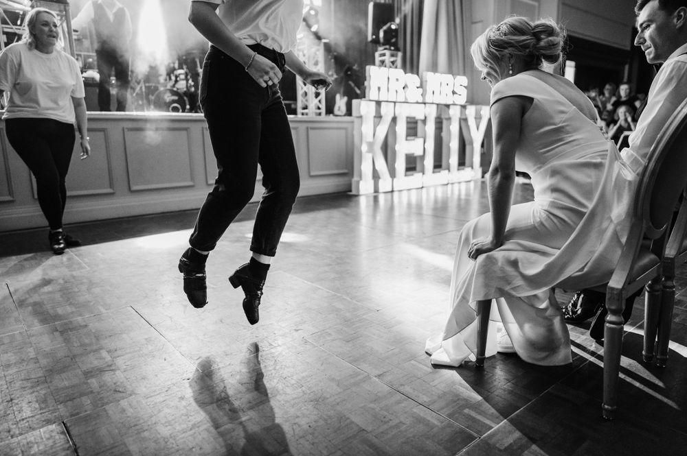 Black and white photo of someone jumping on a dance floor at a wedding reception.