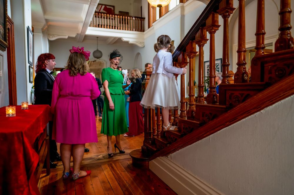 Group in colorful dresses gathered near an elegant wooden staircase during an event.