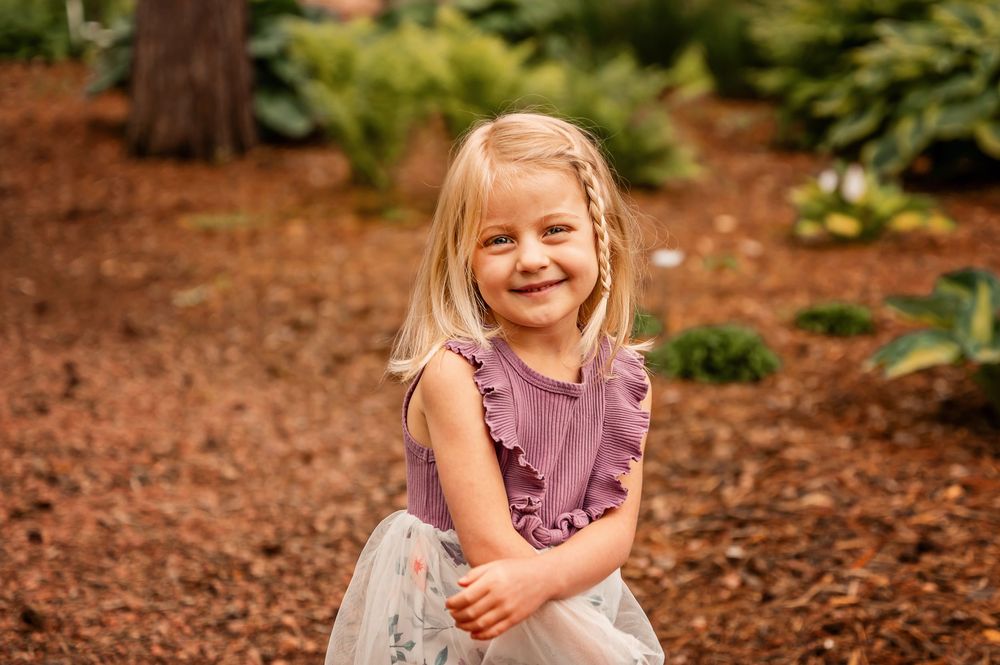 A series of candid outdoor portraits showing a young child playing and laughing in a wooded area with mulch ground cover.
