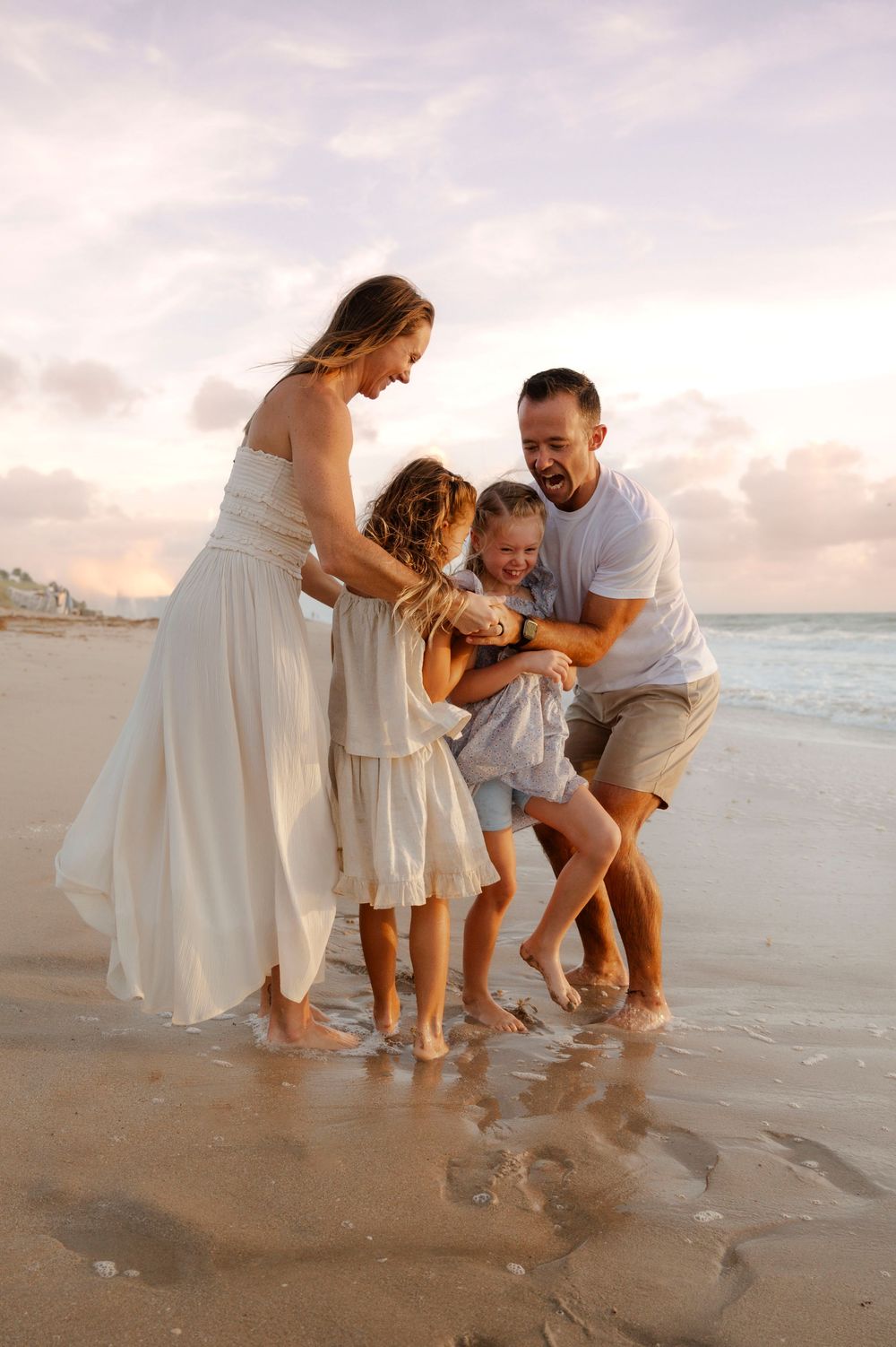 Joyful family of four laughing and playing together in ocean waves at sunset.