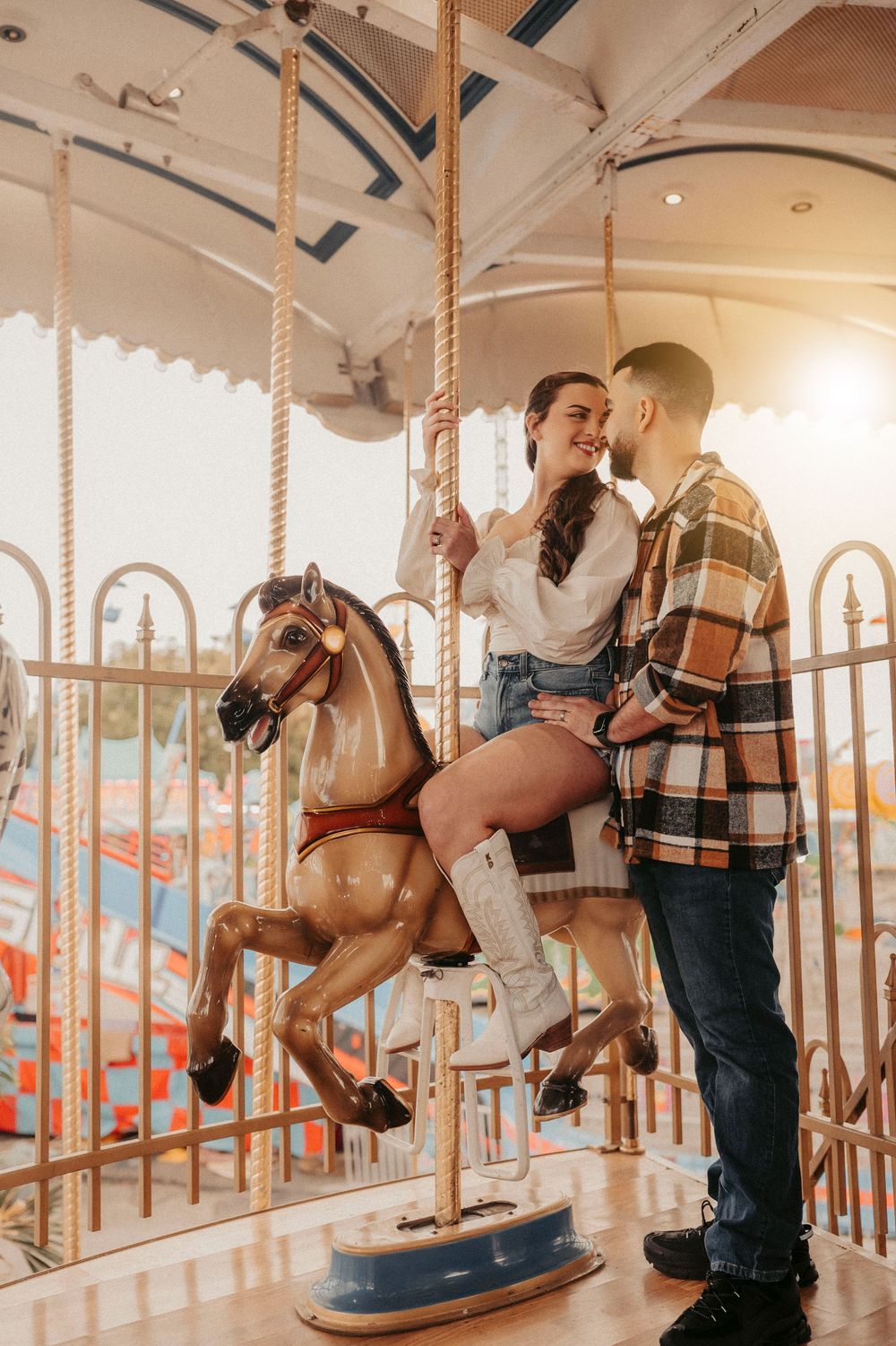 Happy couple on a vintage carousel horse at an amusement park at sunset.