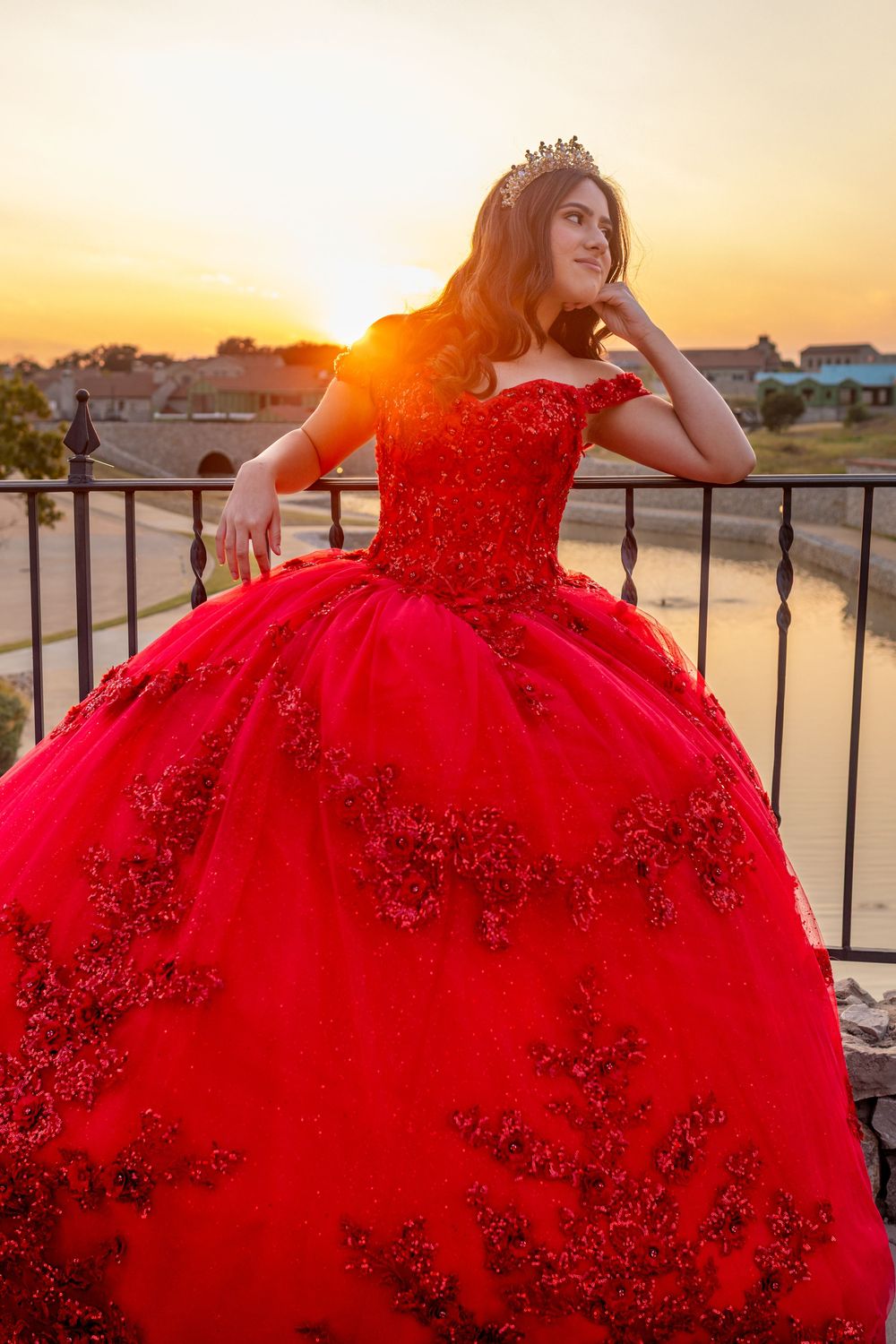 A stunning red XV ballgown with sparkles photographed against a sunset backdrop with iron railings.