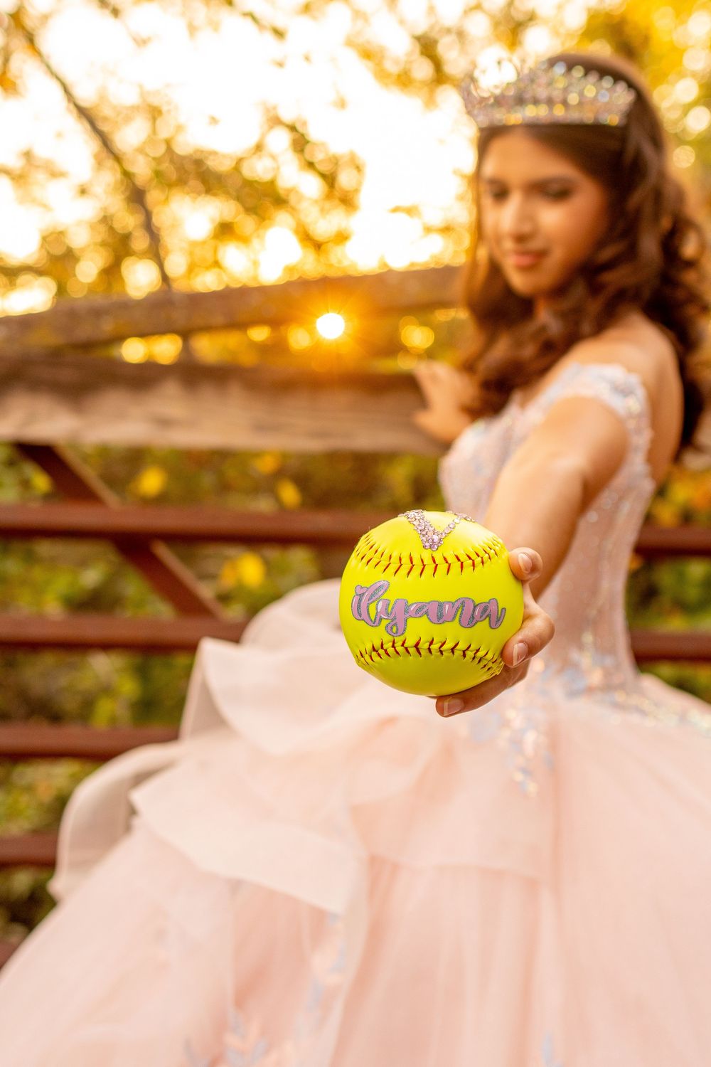 Pink quinceañera dress with yellow softball props in golden sunset lighting.