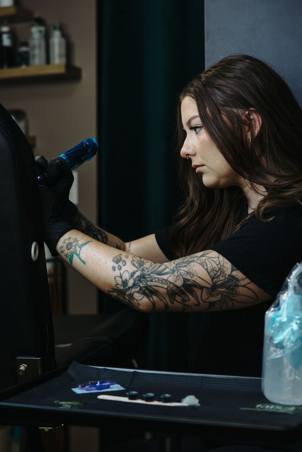 Tattooed female tattoo artist in black gloves working with a tattoo machine in a studio.