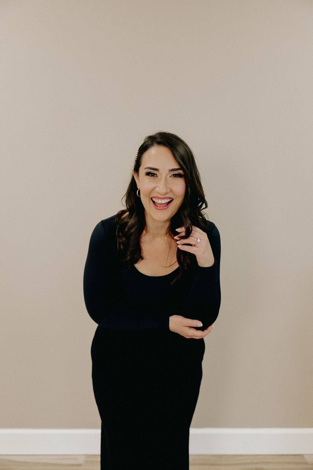 Brunette woman in black dress laughing joyfully against neutral beige studio background.
