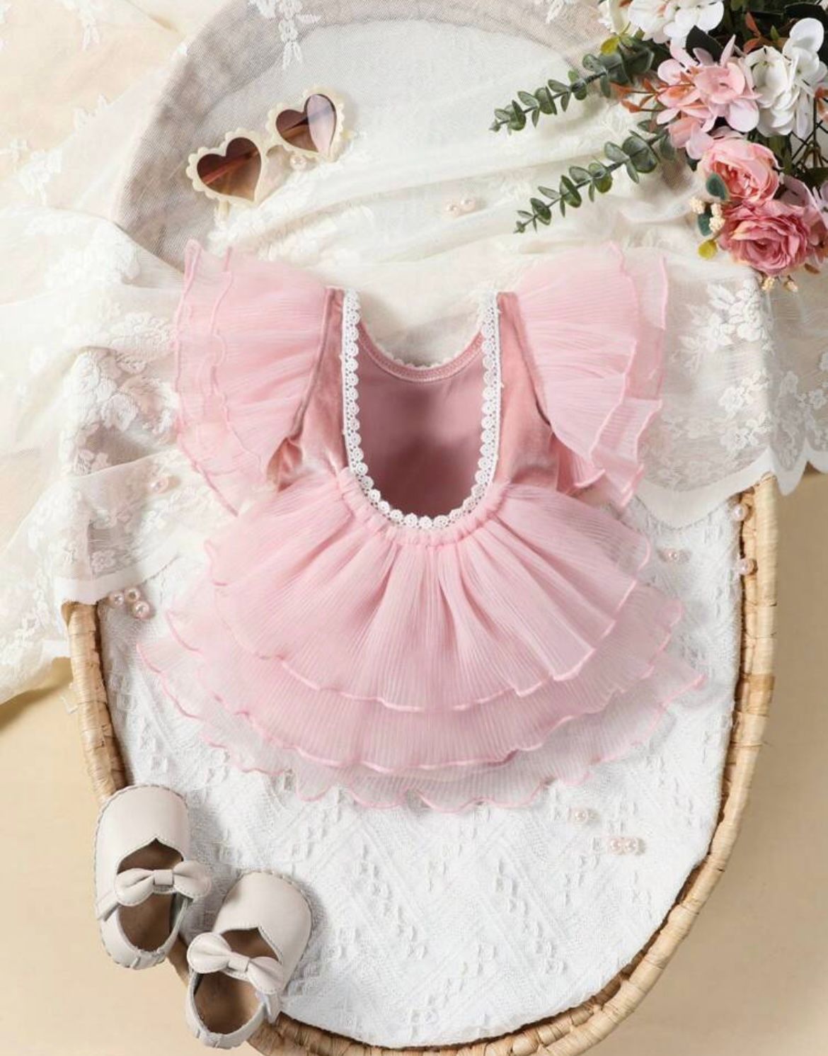 Pink tulle baby dress with ruffles displayed on white textured surface.