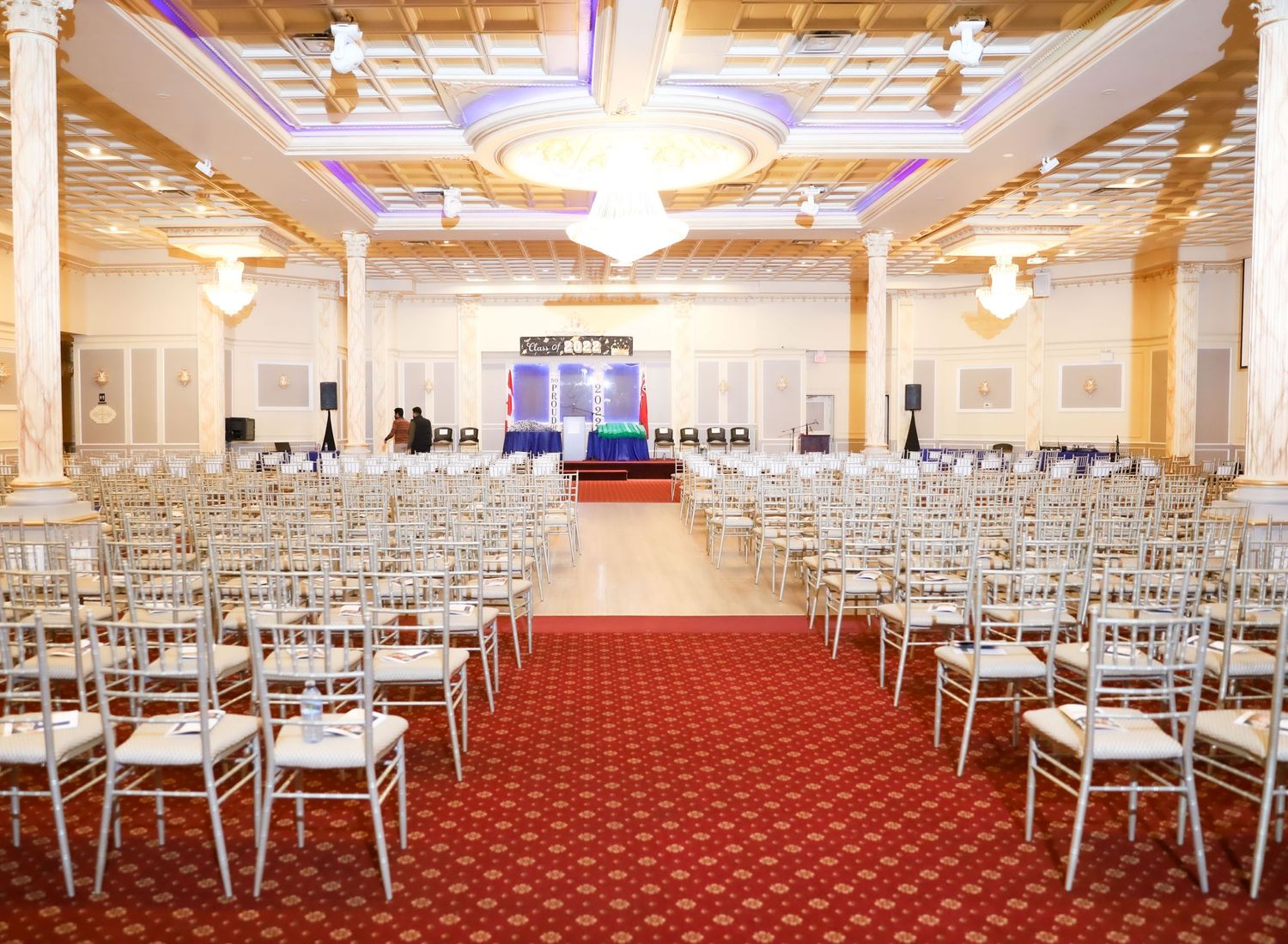 Elegant wedding venue with rows of white chairs, red carpet aisle, and ornate ceiling with chandeliers.