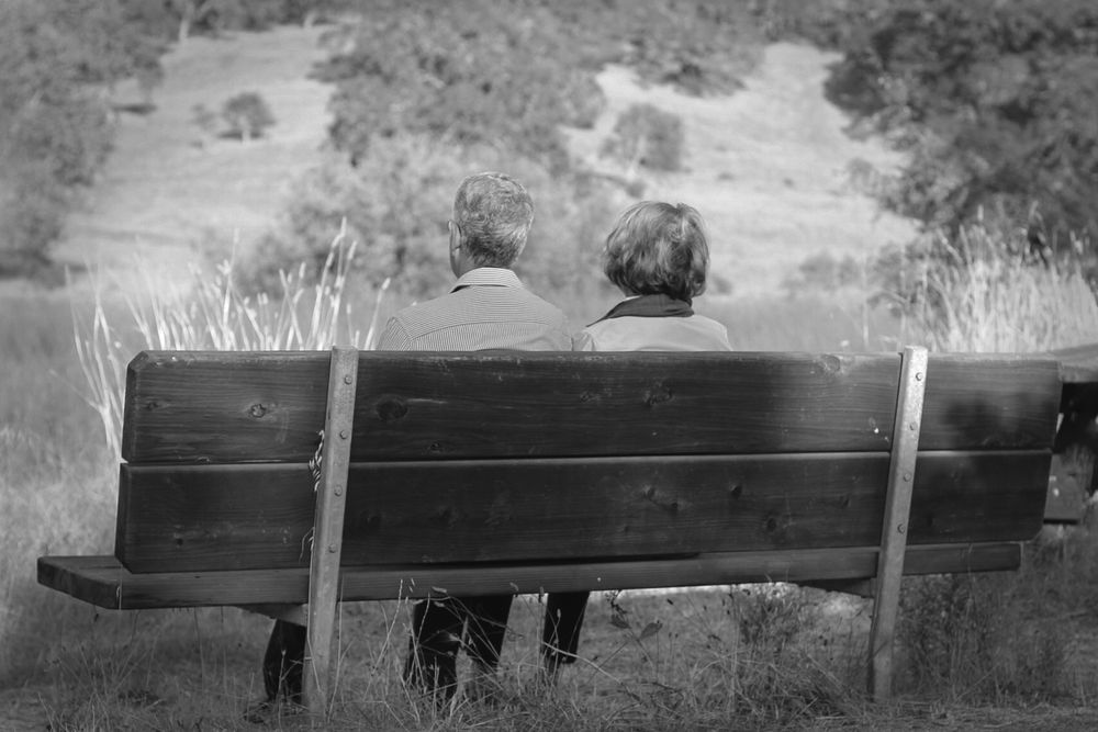 Elderly couple sat together at their favorite bench to rest at when taking walks for 50th anniversary.