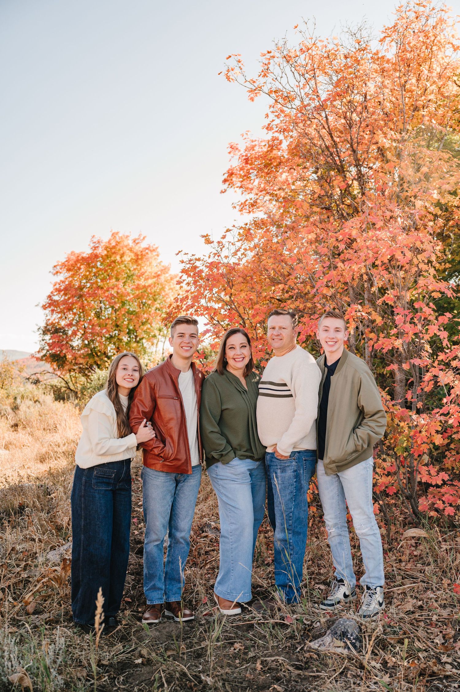 A group stands together outdoors against vibrant orange and red fall foliage on a sunny autumn day.