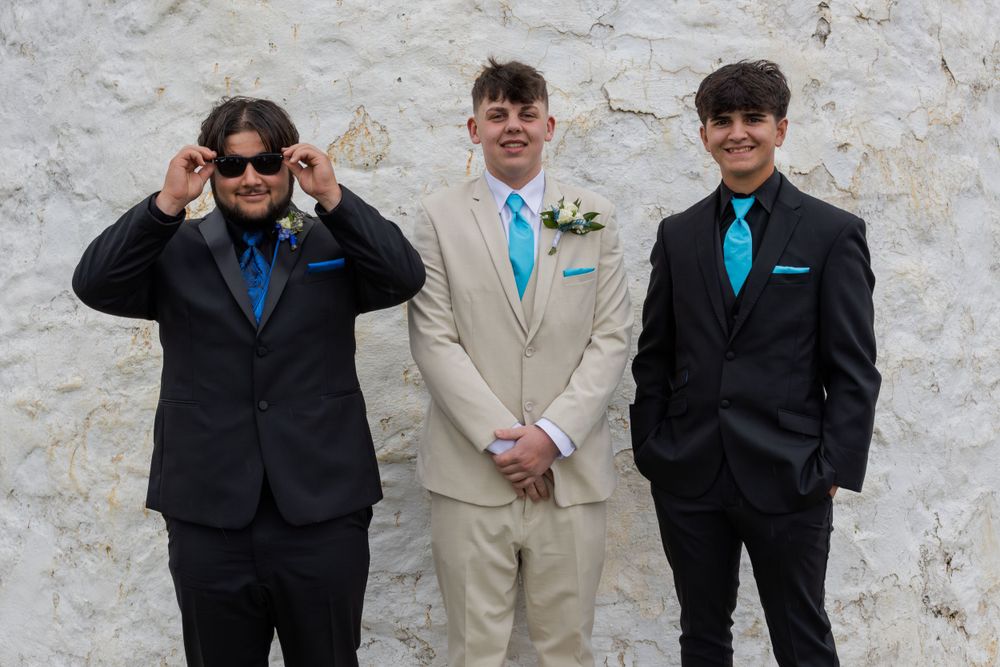 Group in formal wear standing against a light colored stone wall.