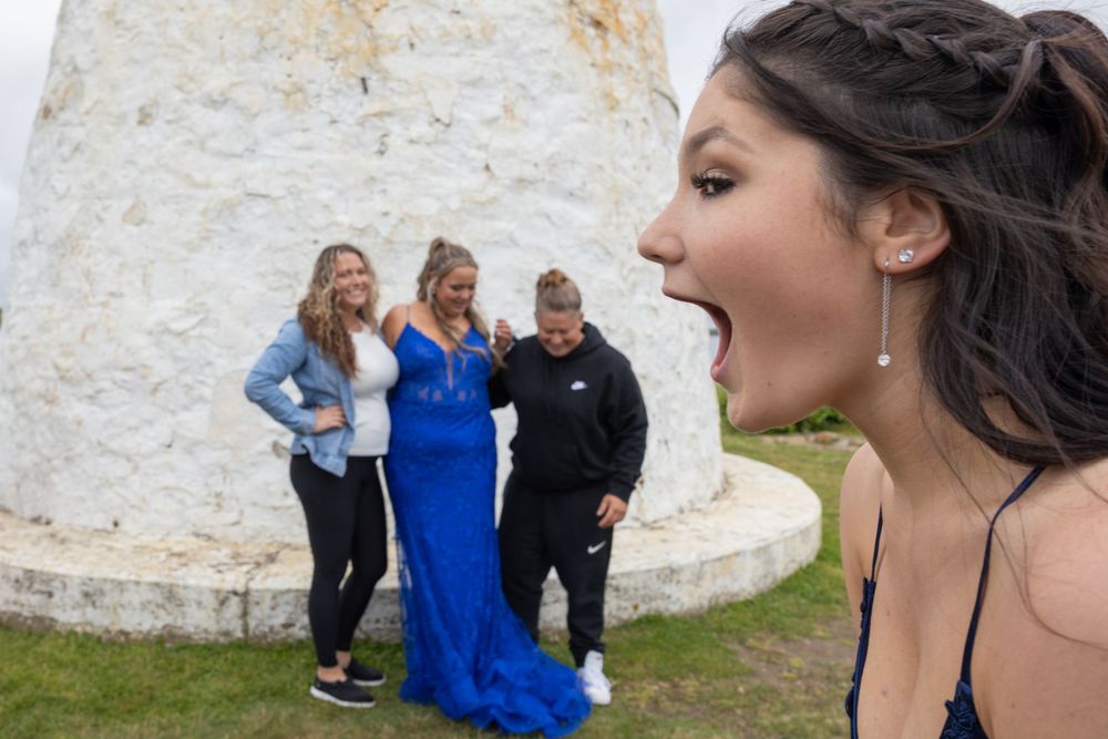People in formal attire posing outdoors near a white stone wall.