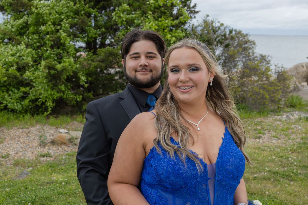 Couple in formal wear posing outdoors near greenery.