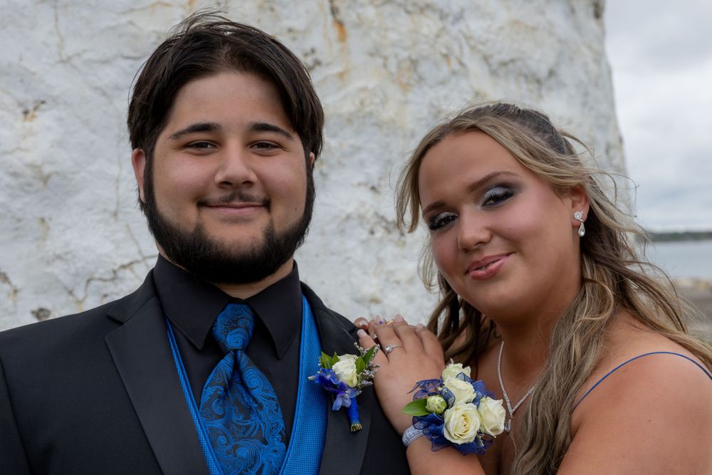 Couple in formal attire posing against a white stone wall.