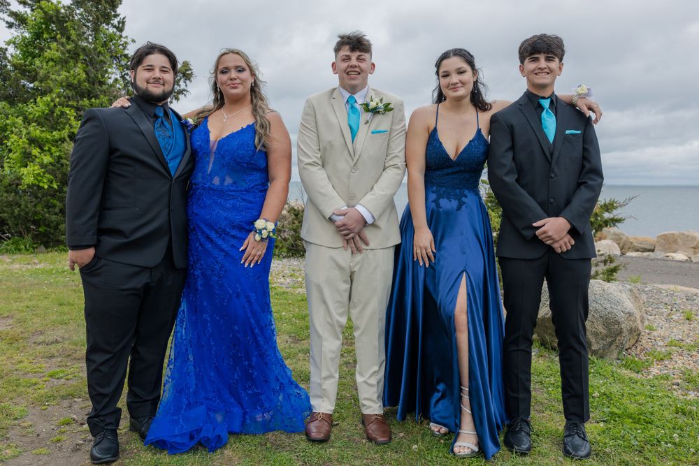 Five people in formal attire stand together outdoors wearing coordinating blue and beige outfits.
