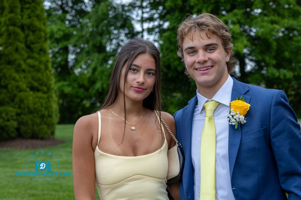 Couple in formal wear with yellow accents pose together at an outdoor event.