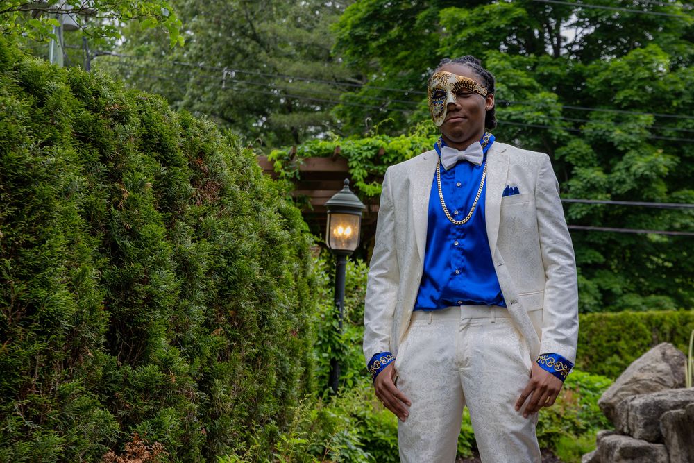 People in formal attire pose outdoors, wearing white suits with blue accents against a green backdrop.