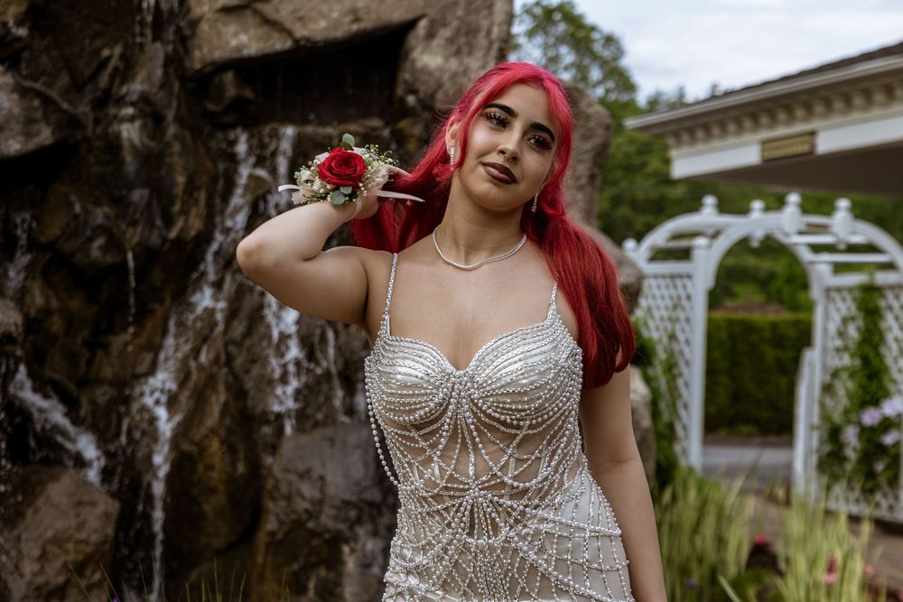 A person in a beaded white dress poses outdoors near a decorative stone wall and garden.