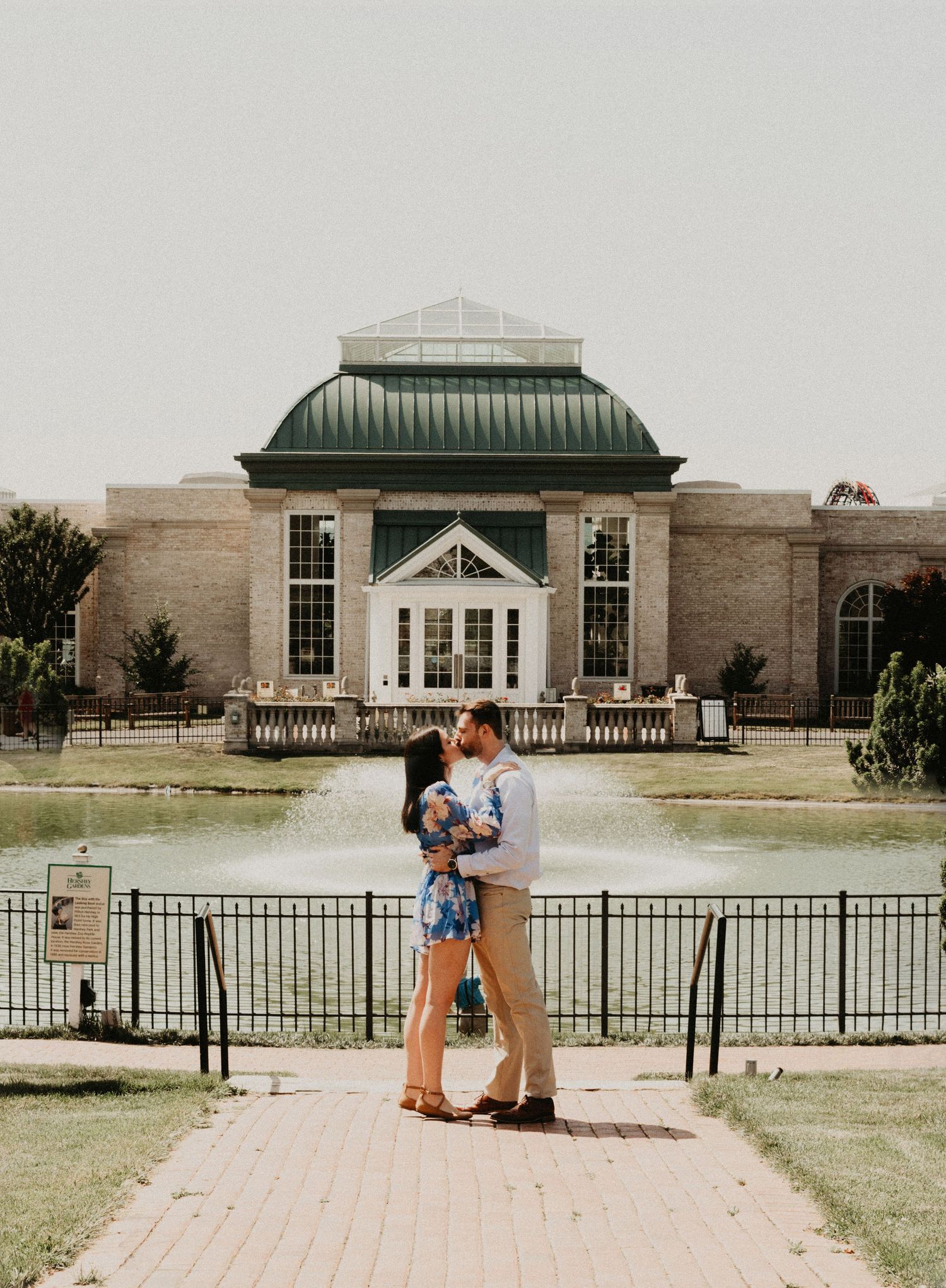 A couple embraces in front of a grand historic building with green roof and white columns.