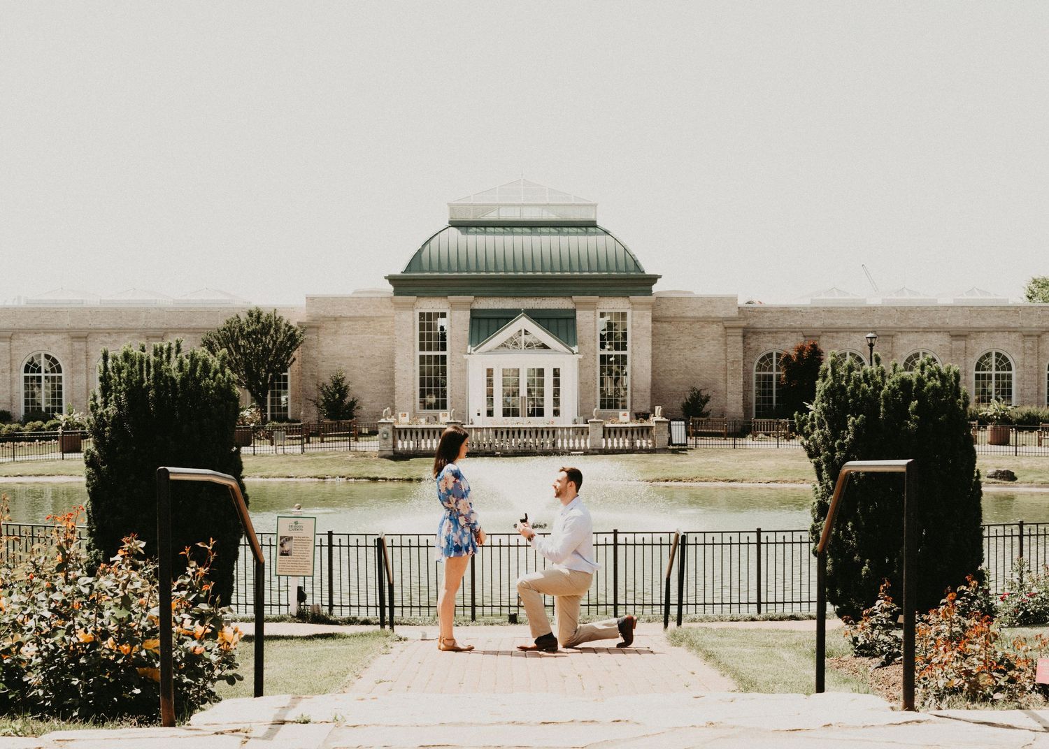 A couple shares a special moment in front of an elegant building with gardens.