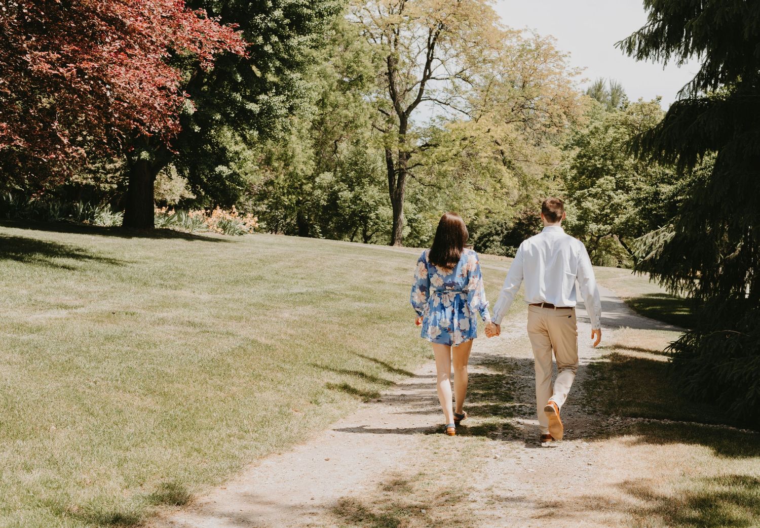 A couple walks hand in hand along a garden path surrounded by lush greenery.