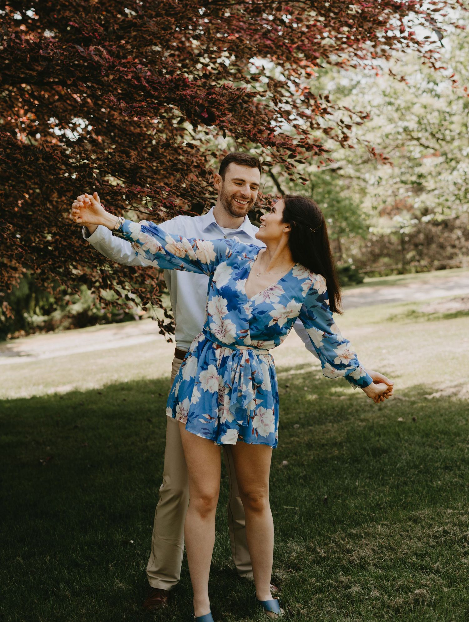A joyful pose in a garden with arms spread wide wearing a blue floral dress.