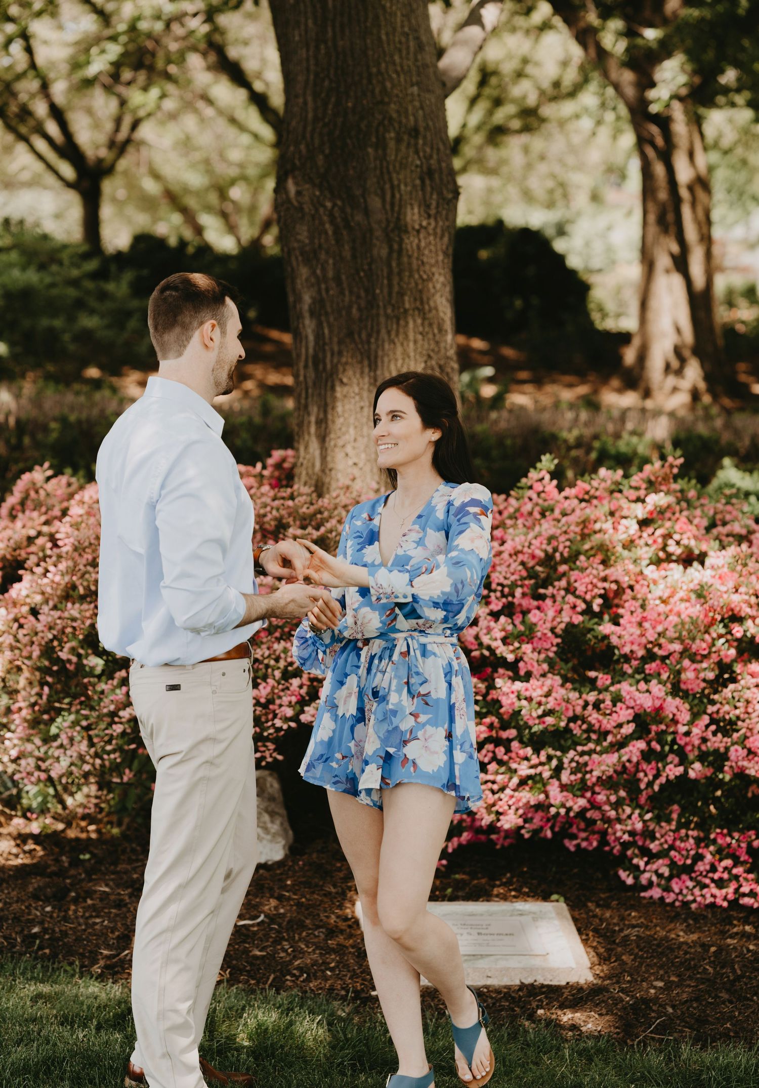 A couple shares a joyful moment among blooming pink azalea flowers.