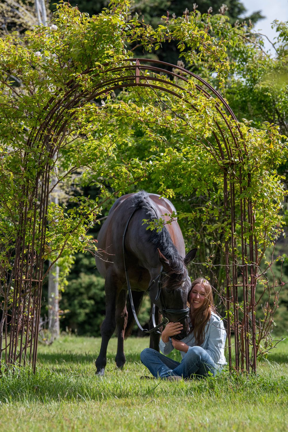 A horse and rider share a tender moment under a flowering tree arch in a green field.