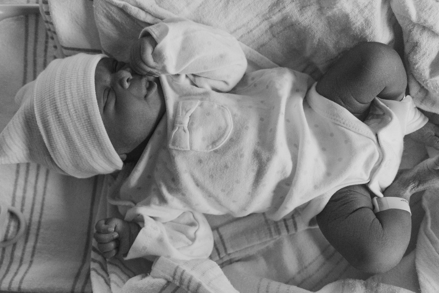 A newborn baby wrapped in white cloth lies peacefully in a hospital setting.