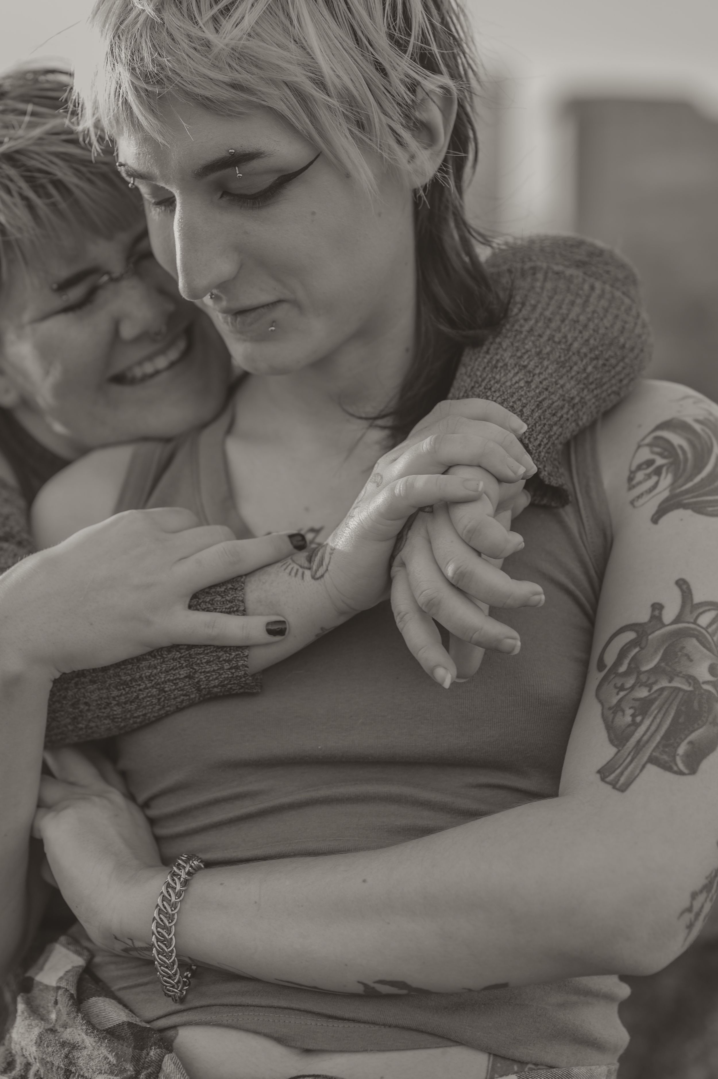 Black and white intimate portrait of a tender embrace showing tattoos and a grey sweater in soft natural lighting.