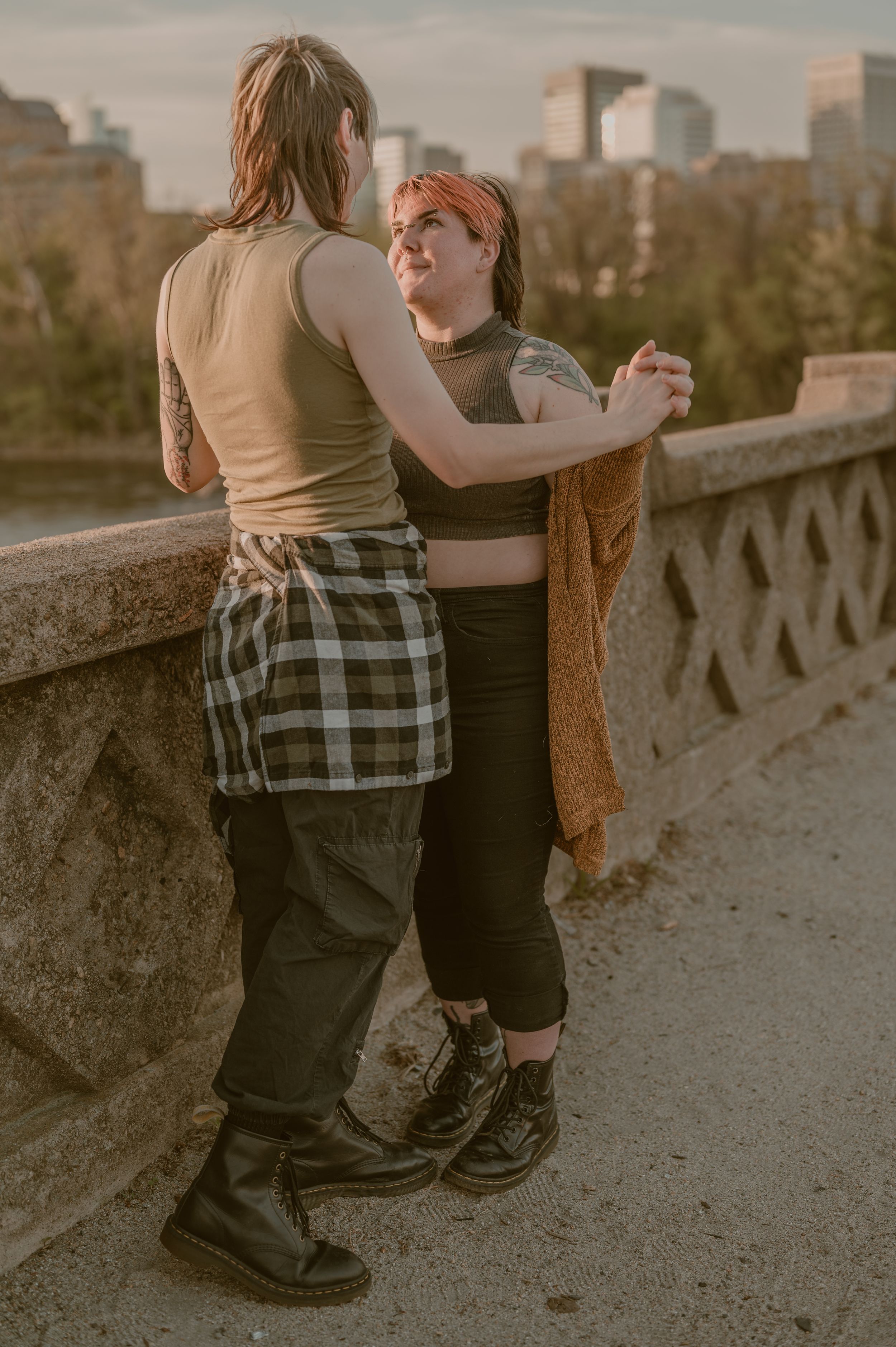 Two people share an intimate moment at sunset on an urban balcony overlooking city buildings in warm golden light.