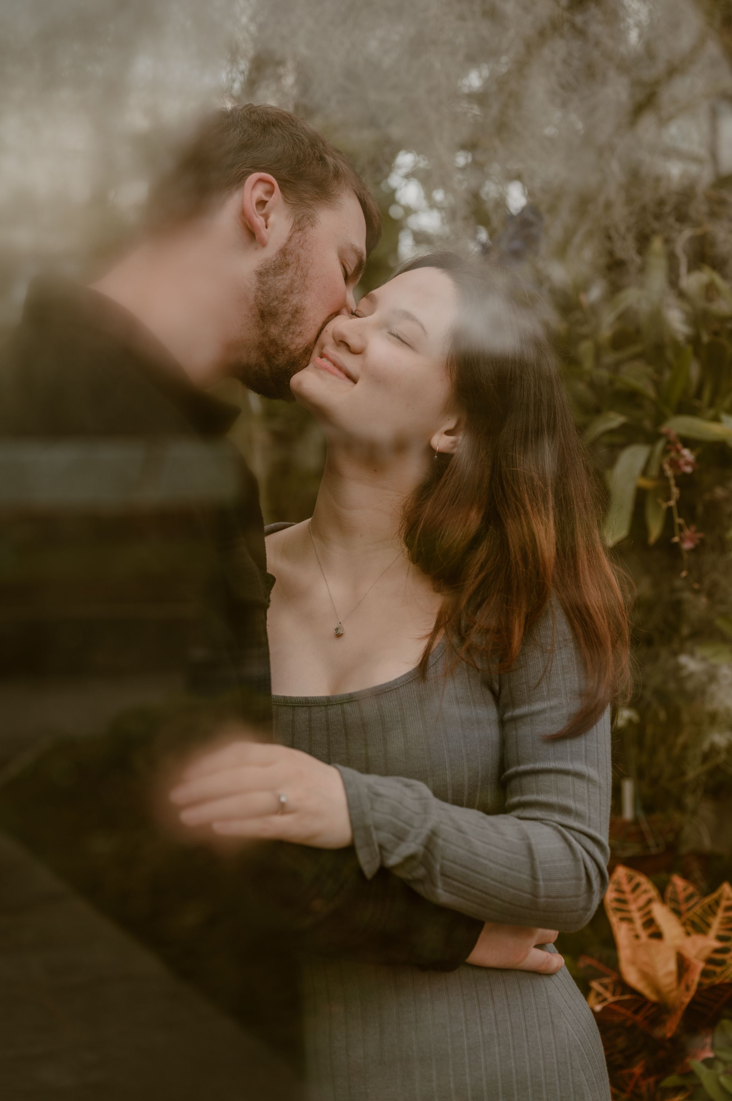 A romantic couple sharing an intimate moment outdoors in soft lighting and natural surroundings in a greenhouse. photo by Samantha Campbell