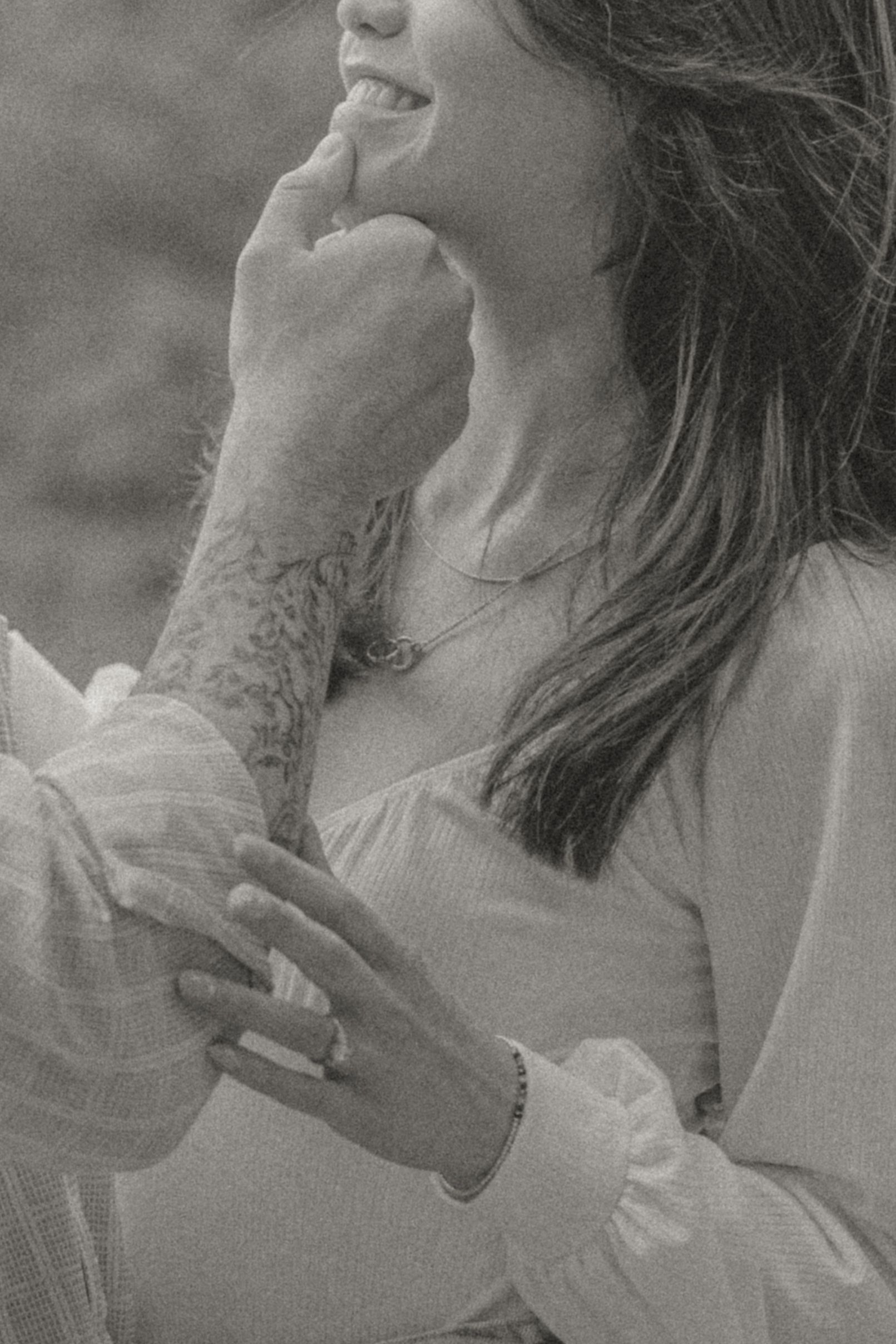 Black and white photo of a couple holding hands, woman smiling with tattoed arm partner.