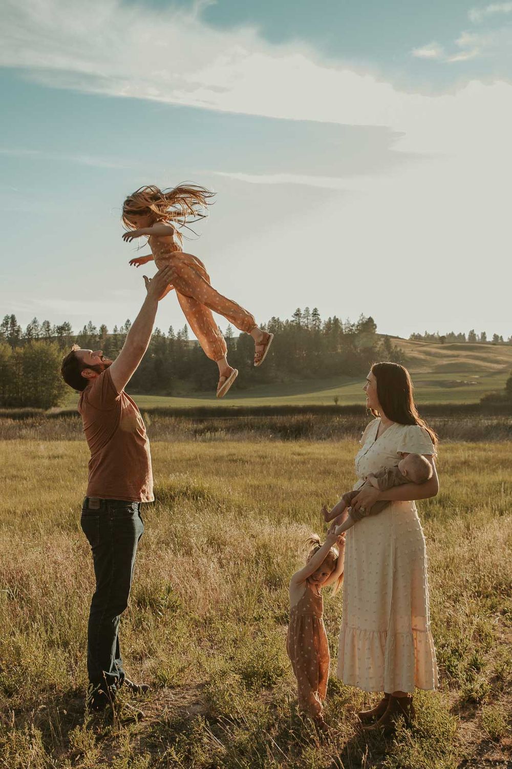 family photo in spokane dad throwing daughter in the air mom and little sister watching from side