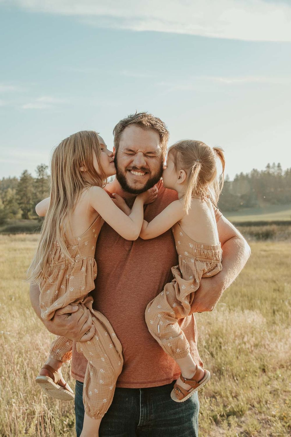 dad in brown shirt holding two daughters with red hair giving kisses on the cheek in spokane