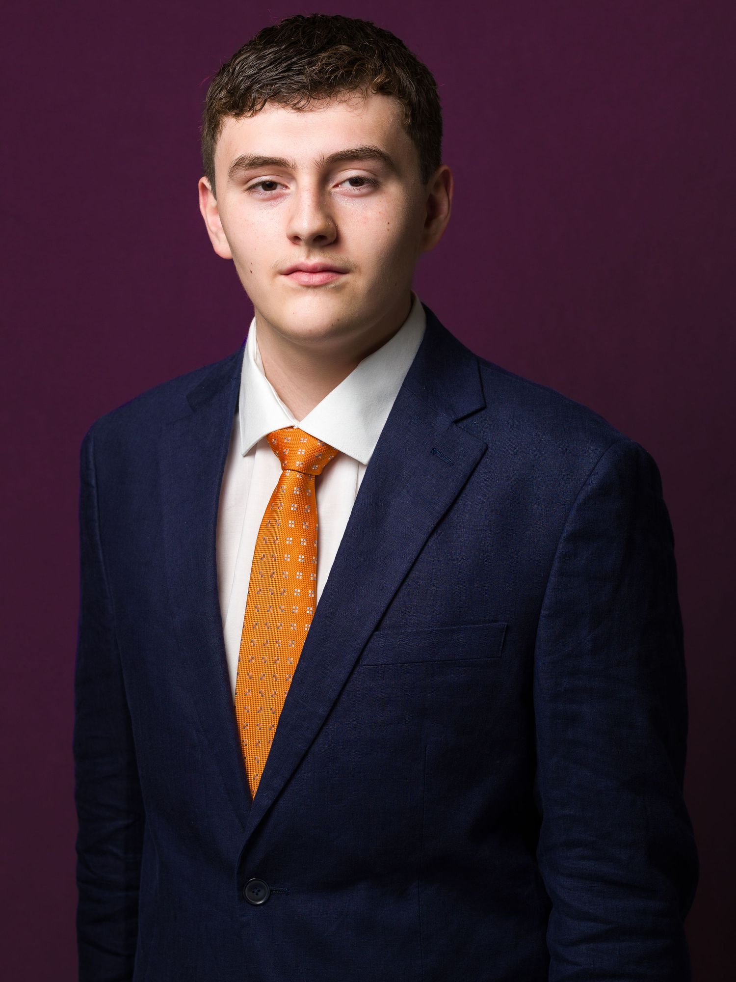 Professional headshot series of person in navy suit and orange tie against dark purple background.