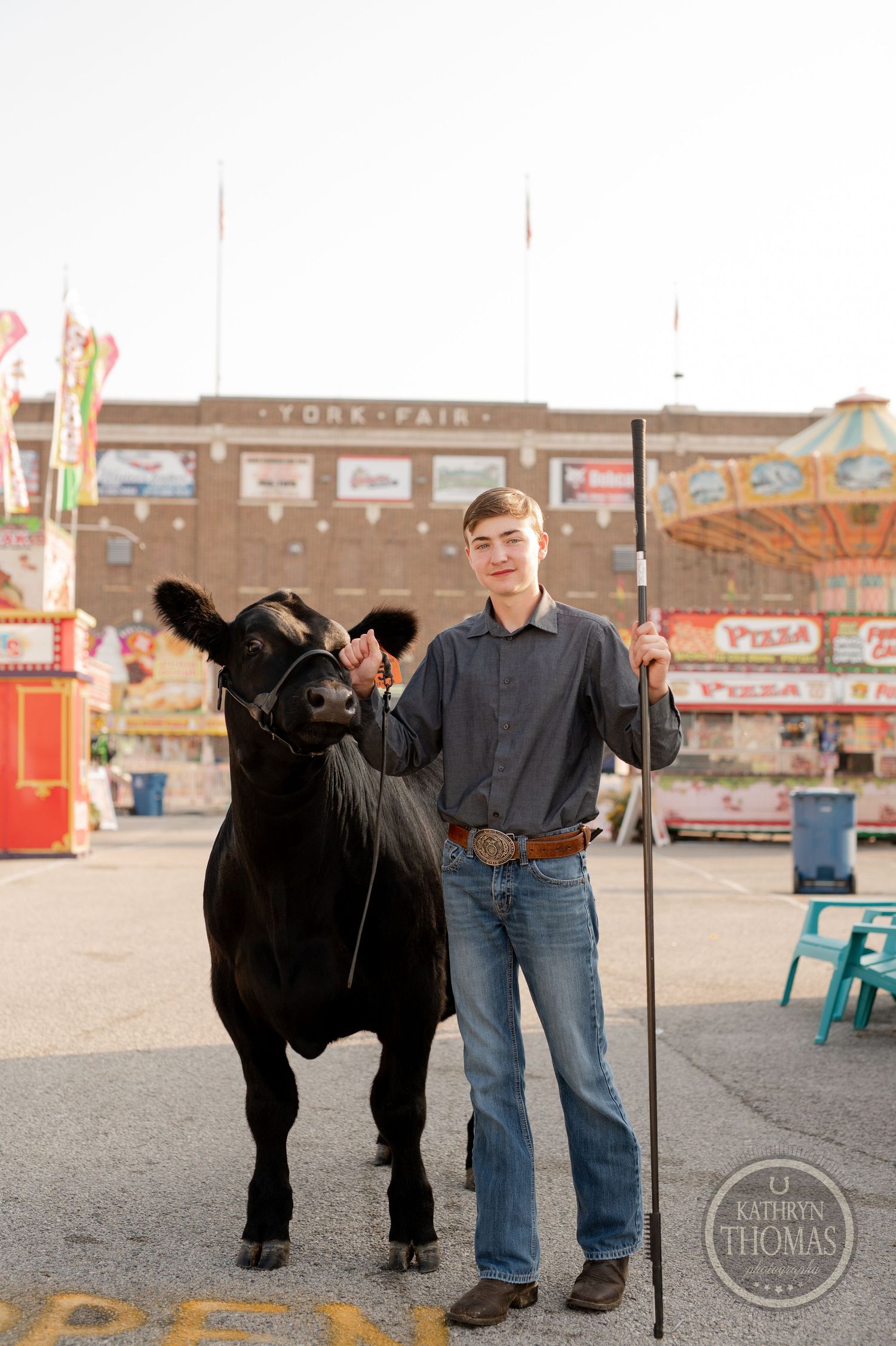 A black show animal looks at camera while standing with handler near carnival booths.