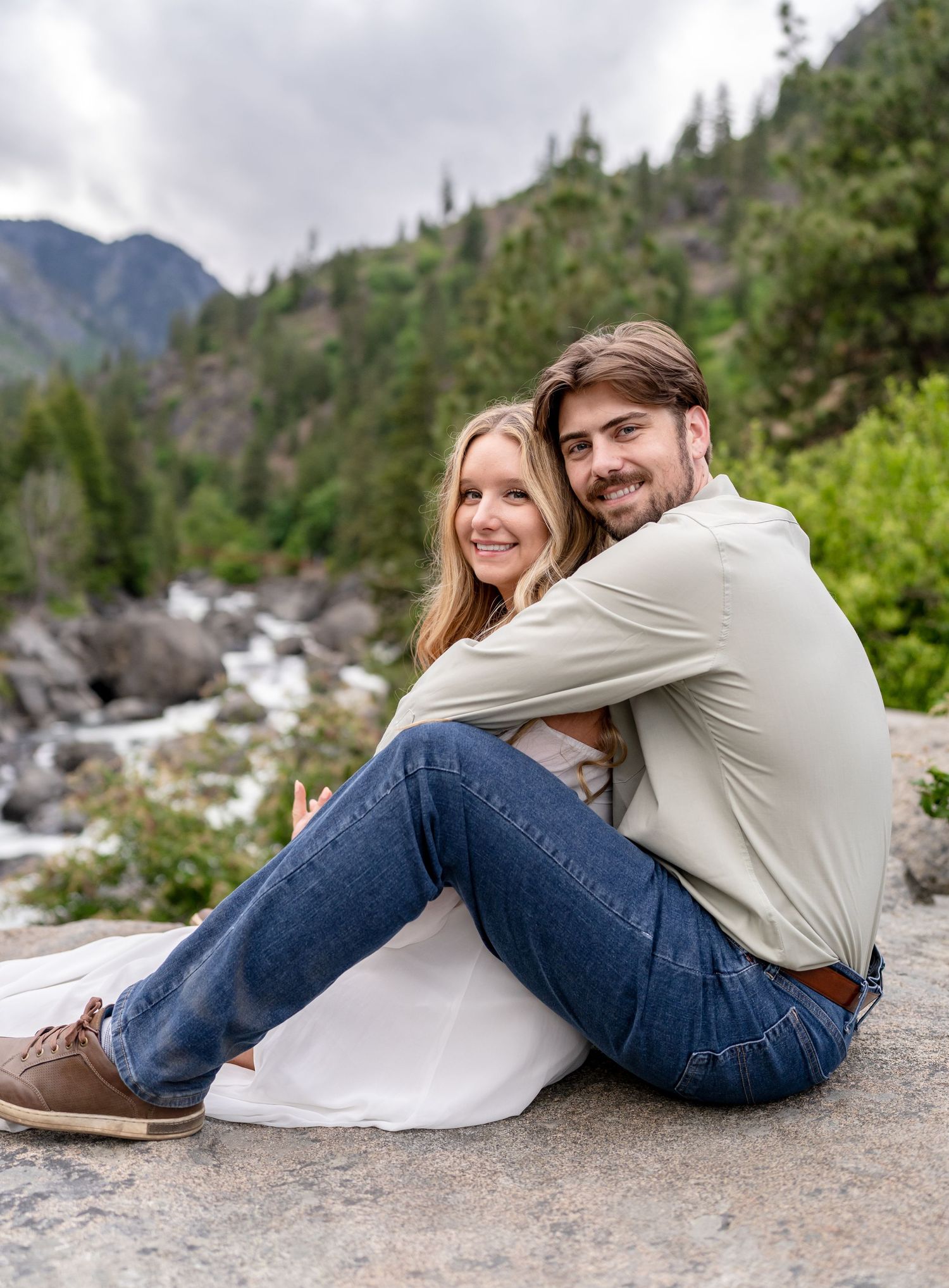 A couple relaxes together on a rocky outcrop overlooking a mountain stream.