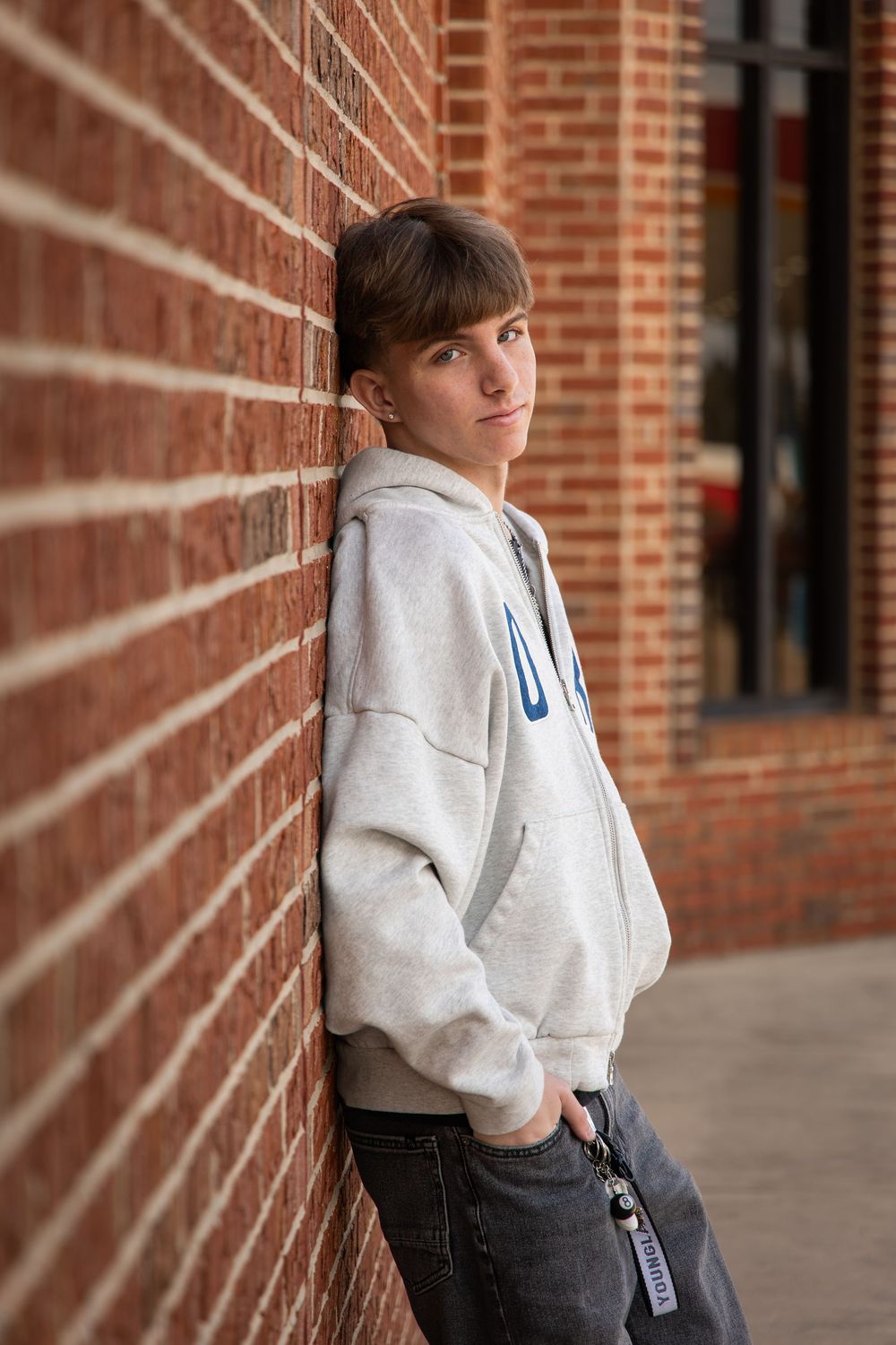 A person in a gray sweatshirt and jeans stands against a brick wall in a series of connected photos.