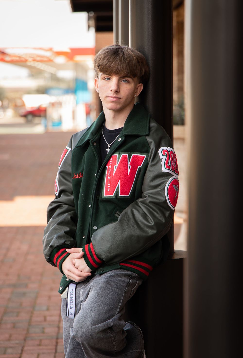 A person in a varsity-style jacket with 'W' lettering poses against a brick wall in a series of outdoor portraits.