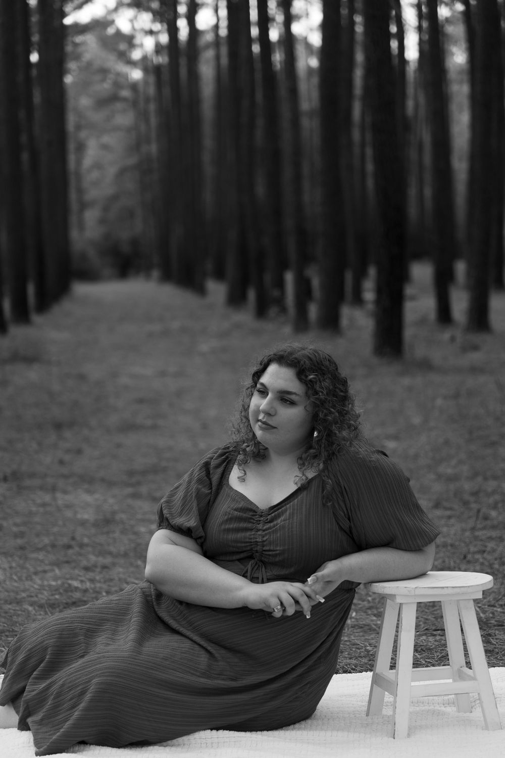 A series of black and white photos showing someone reclining on a white stool in a pine forest setting.