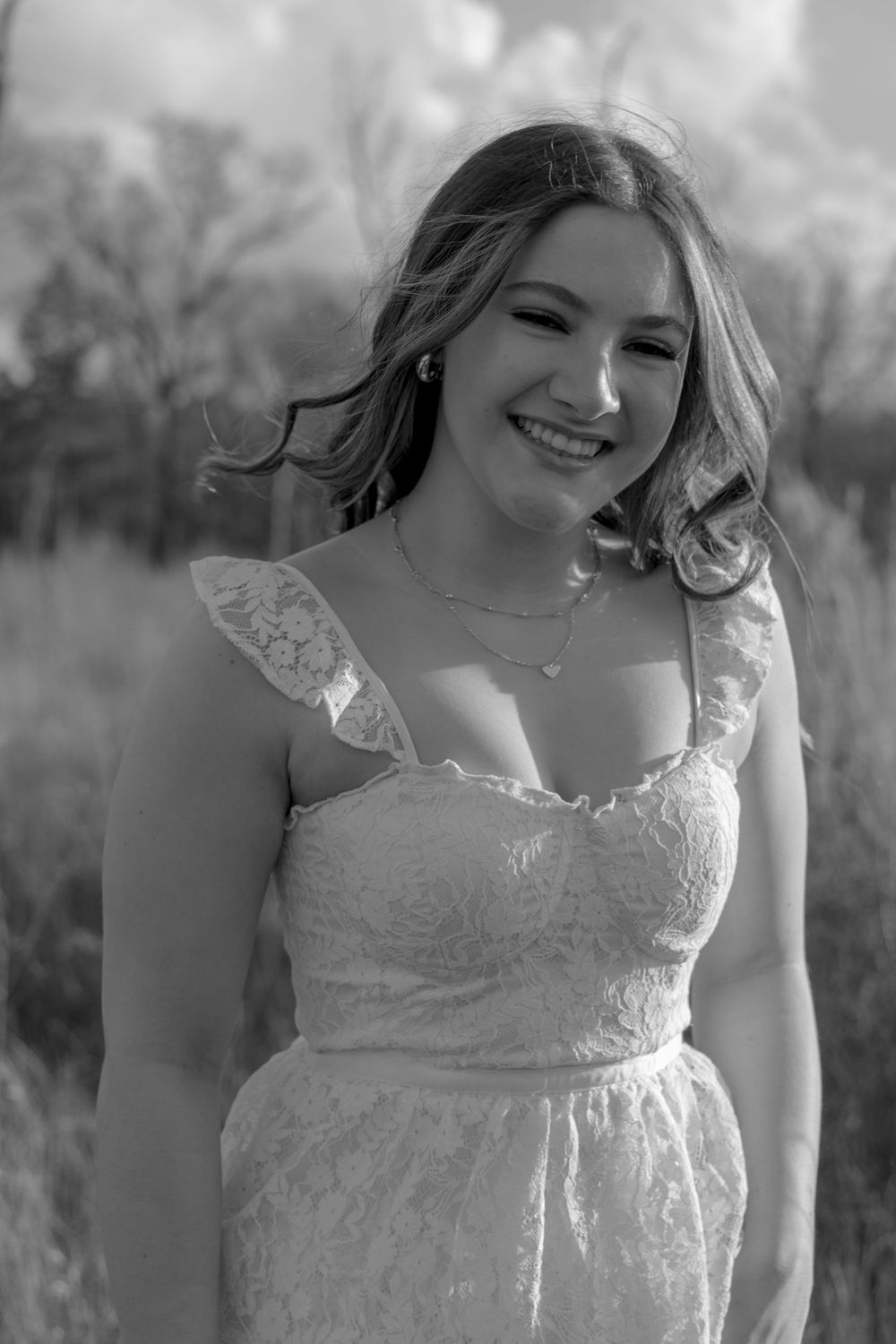 A black and white portrait of someone wearing a delicate lace dress outdoors.