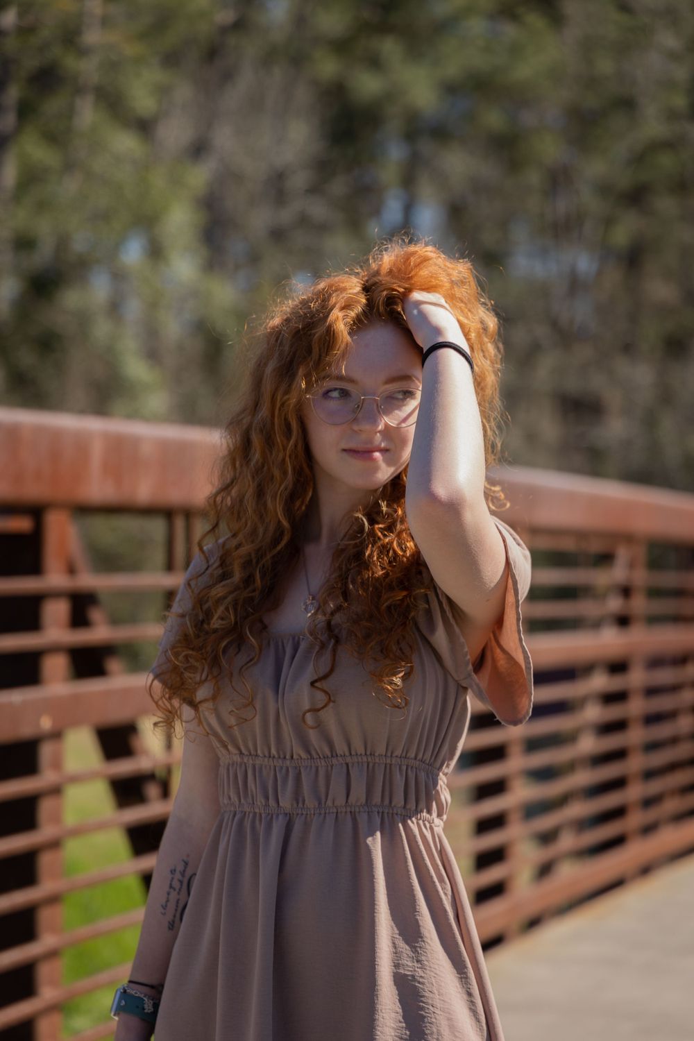 Portrait of someone in a flowy dress posing on wooden bridge in sunlight.