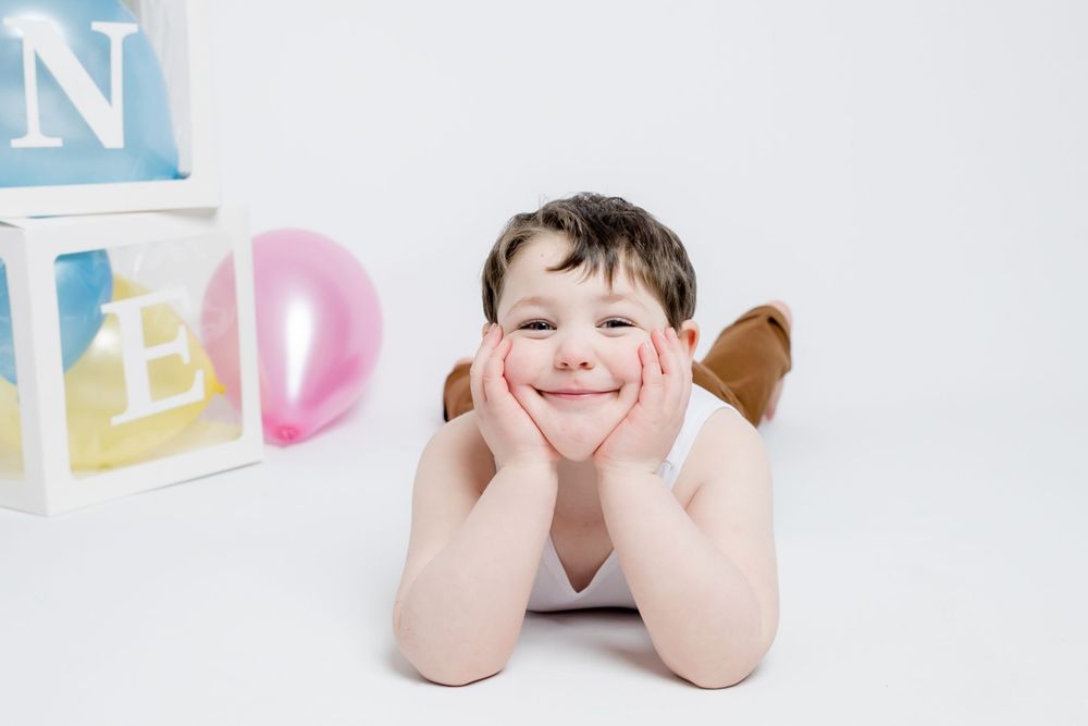 Young child poses in white studio setting with letter blocks in background, hands resting under chin.