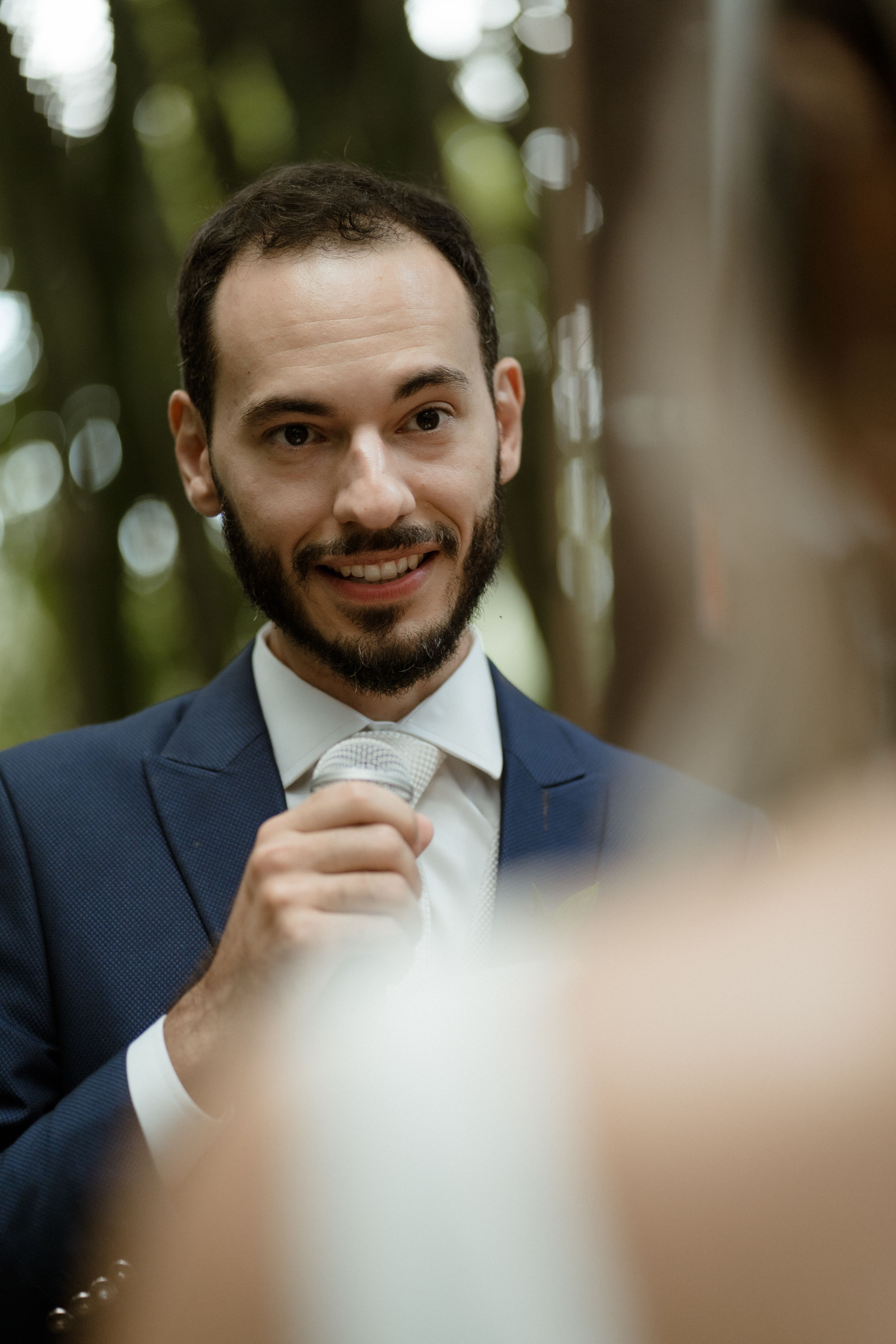 An emotional reaction during wedding vows in a blue suit against a forest backdrop.